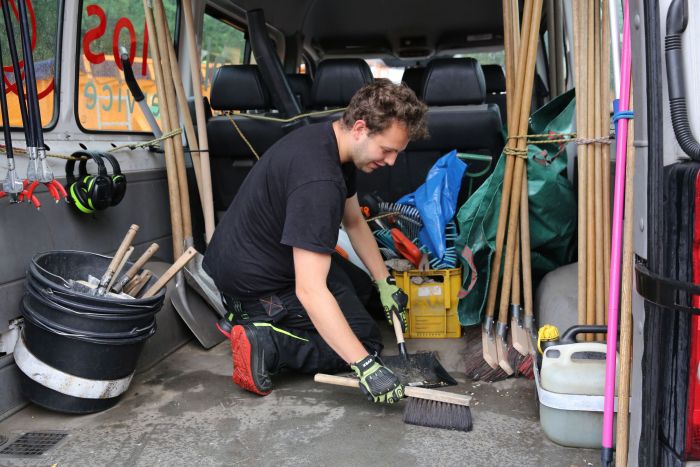 Ein junger Mann kehrt und kniet inmitten der Werkzeuge im Auto