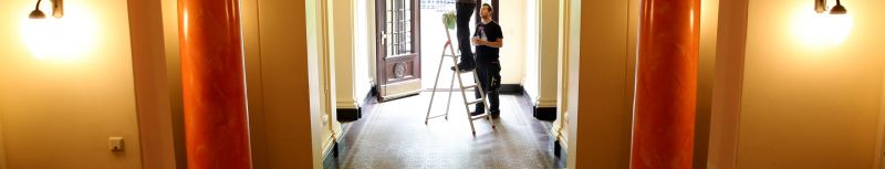 Zwei Mitarbeiter von Hausmeisterservice Problemlos stehen auf der Leiter in einem Flur und reparieren eine Lampe