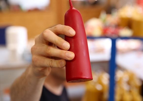 Eine Hand hält eine rote Kerze in die Kamera, erstellt in unserer Kerzenmanufaktur