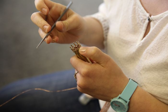 Hände einer Künstlerin aus unserer Designwerkstatt halten einen goldenen Gegenstand