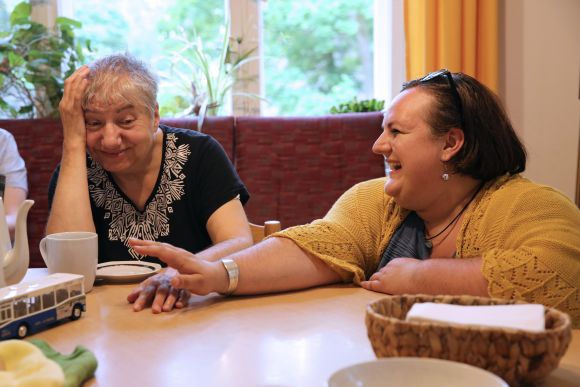 Zwei Frauen sitzen am Tisch und lachen.