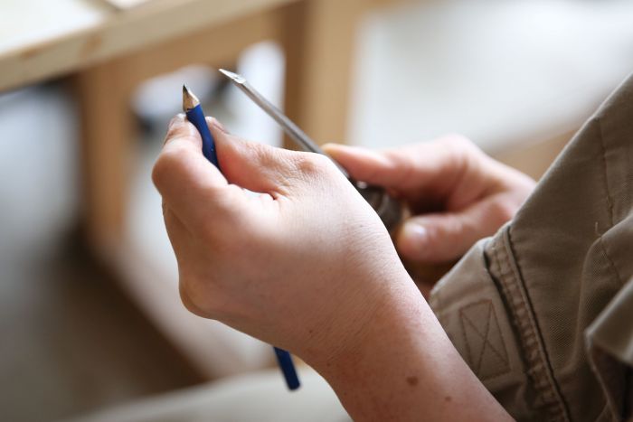 Hände eines Tischlers, der einen blauen Bleistift spitzt