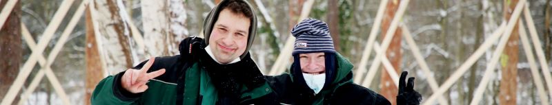 Zwei Mitarbeiter der Forstgruppe in grüner Winterkleidung zeigen Victory-Zeichen in die Kamera und lachen fröhlich