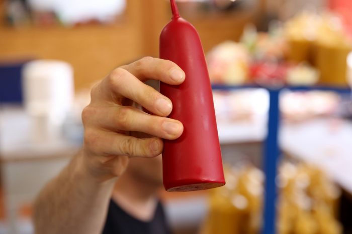 Eine Hand hält eine rote Kerze in die Kamera, erstellt in unserer Kerzenmanufaktur