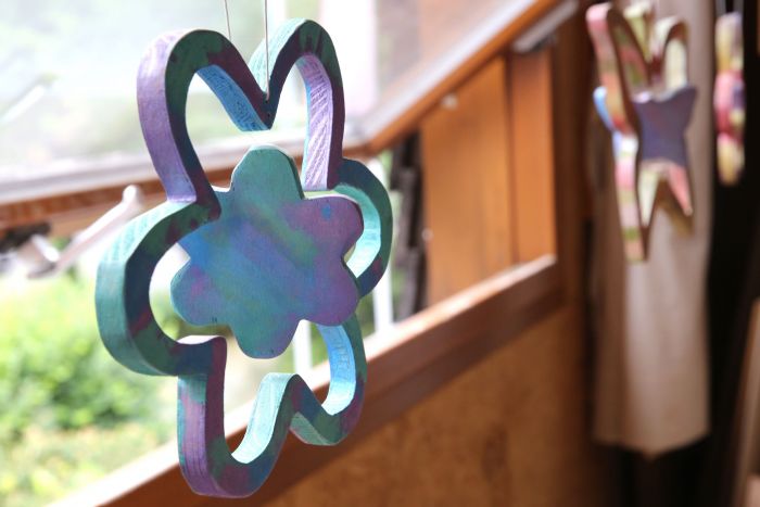 Ein blaues Blumen-Mobile aus Holz am Fenster hängend, ein Kunstwerk aus unserer Tischlerei