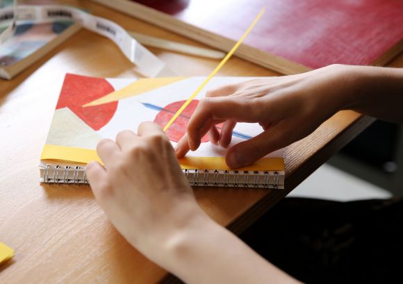 Hände einer Mitarbeiterin, die ein Büchlein bindet in unserer Papierwerkstatt