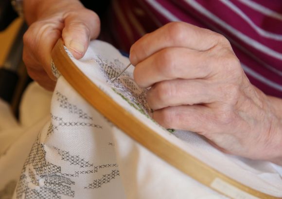 Die Hand einer älteren Frau, die stickt