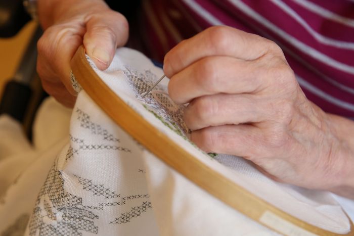 Die Hand einer älteren Frau, die stickt
